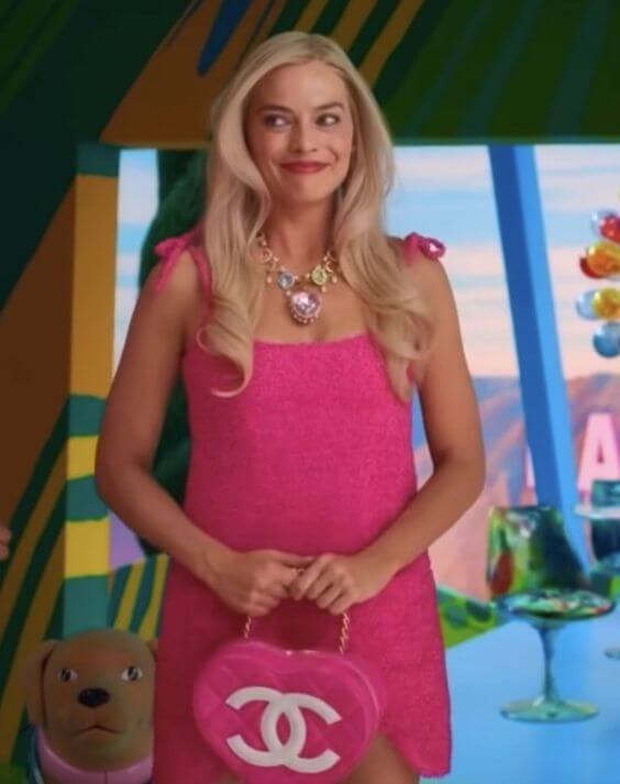 A picture of Margot Robbie as Barbie in a pink dress, jewelled necklace and chanel heart shaped bag.