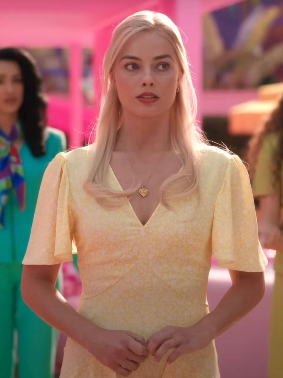 A picture of Margot Robbie as Barbie in a yellow dress and gold heart necklace.