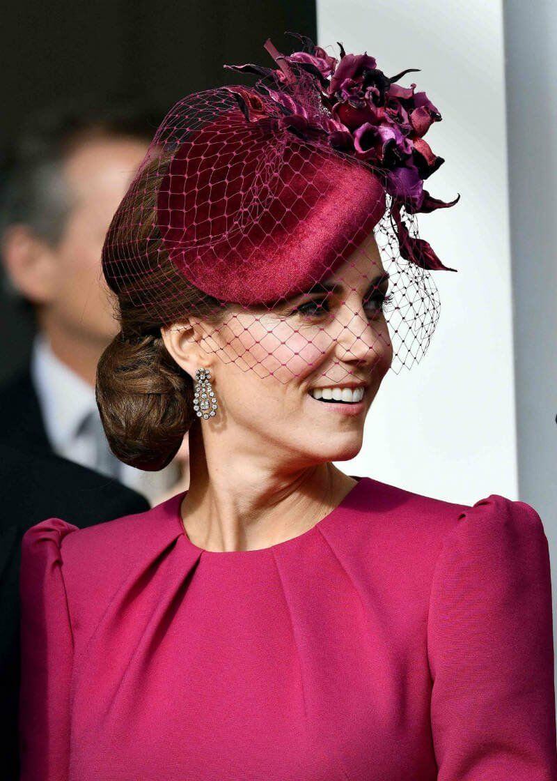 A picture of Duchess Catherine Middleton in a dark pink veiled fascinator.